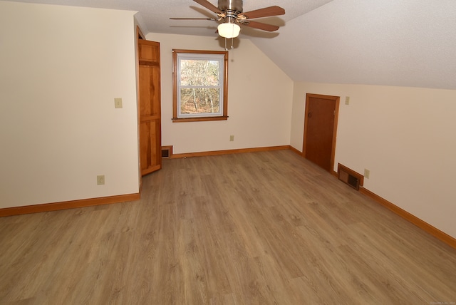 additional living space with a textured ceiling, ceiling fan, lofted ceiling, and light wood-type flooring