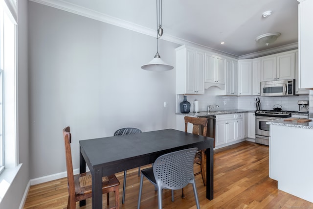 kitchen with light stone countertops, appliances with stainless steel finishes, decorative light fixtures, white cabinets, and light wood-type flooring