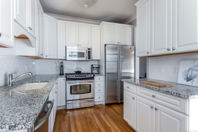 kitchen featuring light stone countertops, appliances with stainless steel finishes, sink, wood-type flooring, and white cabinets