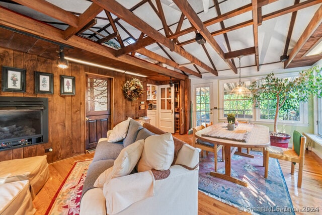 living room featuring lofted ceiling with beams, wood walls, and light wood-type flooring