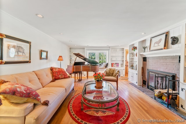 living room featuring a brick fireplace, light hardwood / wood-style flooring, built in shelves, and ornamental molding