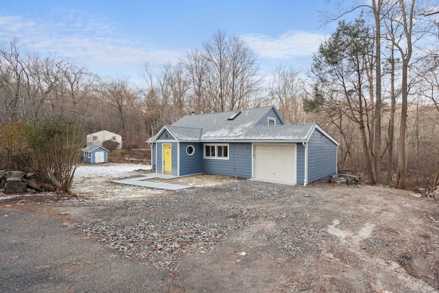 exterior space featuring a shingled roof, a detached garage, dirt driveway, a storage shed, and an outbuilding