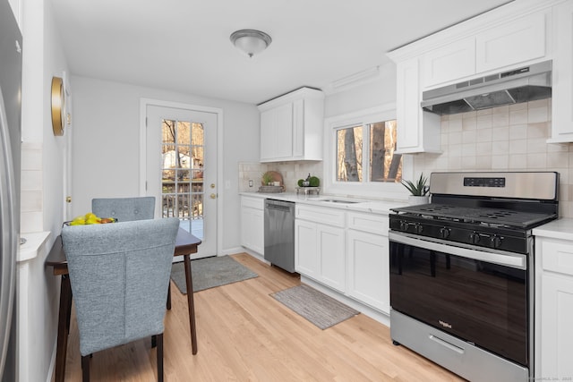 kitchen with stainless steel appliances, light countertops, under cabinet range hood, light wood-type flooring, and backsplash