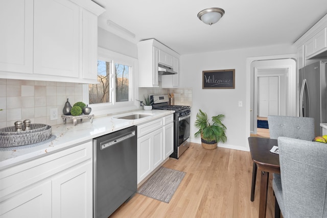 kitchen featuring light stone counters, light wood finished floors, a sink, appliances with stainless steel finishes, and white cabinetry