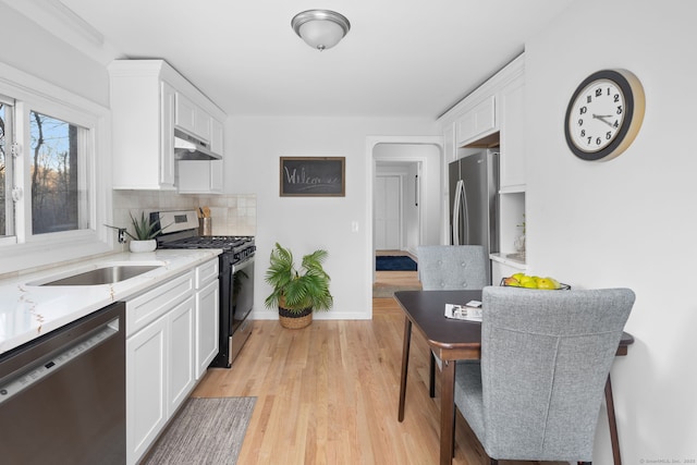 kitchen with under cabinet range hood, decorative backsplash, stainless steel appliances, white cabinetry, and a sink