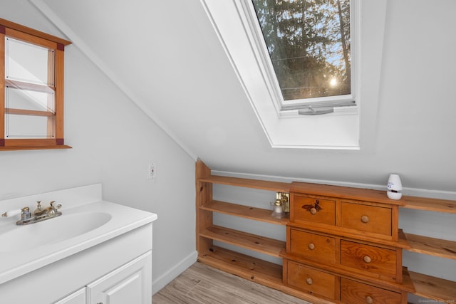 bathroom with vanity, vaulted ceiling with skylight, wood finished floors, and baseboards