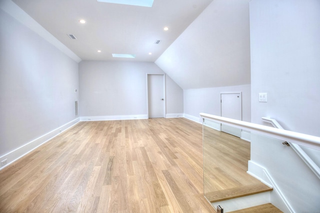 additional living space with vaulted ceiling with skylight and light wood-type flooring