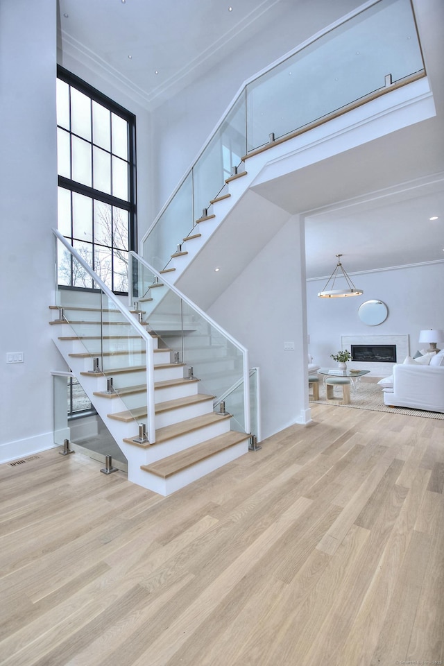 stairway featuring hardwood / wood-style flooring, crown molding, a towering ceiling, and a chandelier