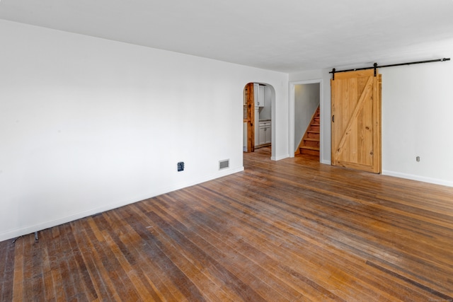 unfurnished room with a barn door and dark wood-type flooring