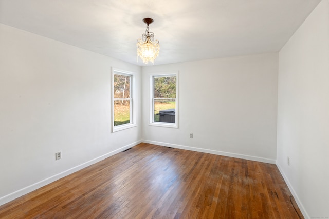 spare room with a chandelier and dark hardwood / wood-style floors