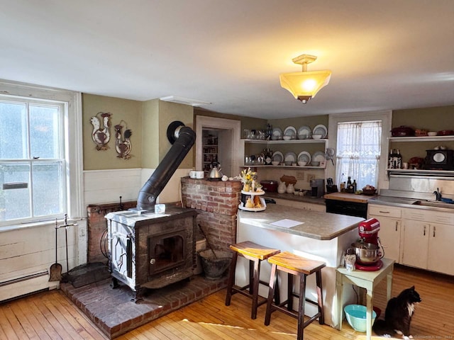 kitchen with white cabinets, light wood-type flooring, a wood stove, and a wealth of natural light