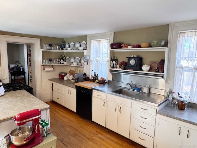 kitchen with white cabinetry, sink, stainless steel counters, black dishwasher, and light hardwood / wood-style flooring