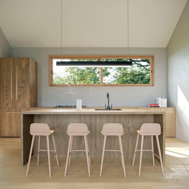 kitchen with a kitchen breakfast bar, sink, vaulted ceiling, and light wood-type flooring