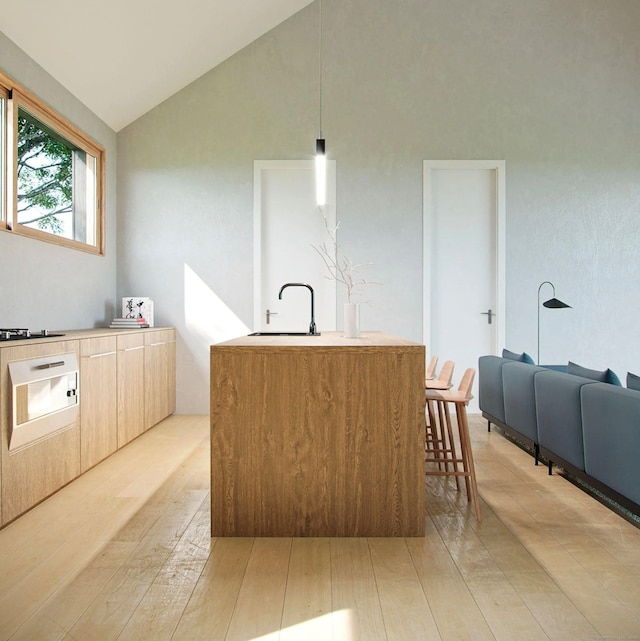 kitchen featuring sink, a center island with sink, decorative light fixtures, light hardwood / wood-style flooring, and lofted ceiling