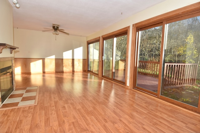 unfurnished sunroom featuring ceiling fan, a tile fireplace, and a wealth of natural light