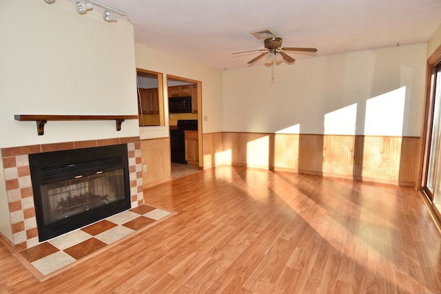 unfurnished living room featuring a fireplace, ceiling fan, light hardwood / wood-style flooring, and wooden walls