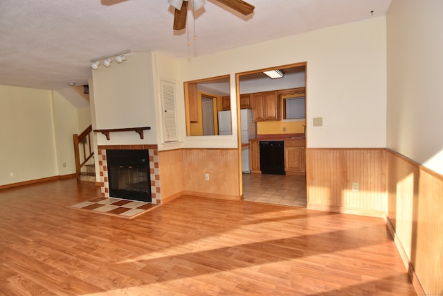 unfurnished living room with ceiling fan, wood walls, a textured ceiling, and light hardwood / wood-style flooring