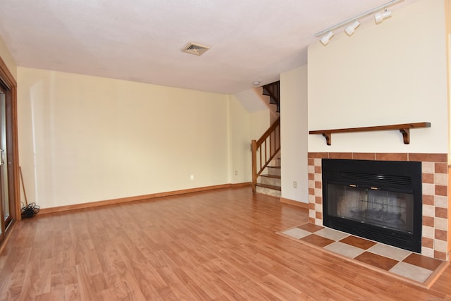 unfurnished living room featuring a fireplace, rail lighting, and wood-type flooring