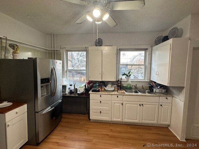 kitchen with white cabinets, stainless steel fridge, light hardwood / wood-style flooring, and sink