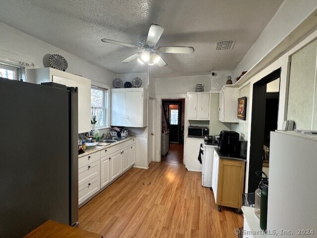 kitchen with a textured ceiling, light wood-type flooring, stainless steel appliances, and white cabinetry