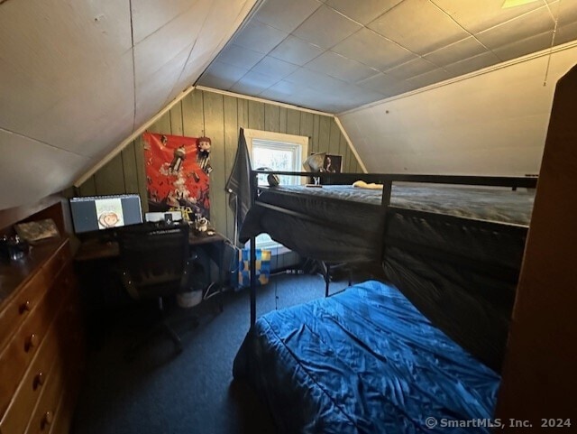 carpeted bedroom featuring wood walls and lofted ceiling