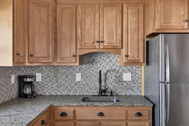 kitchen with decorative backsplash, sink, light stone countertops, and stainless steel refrigerator