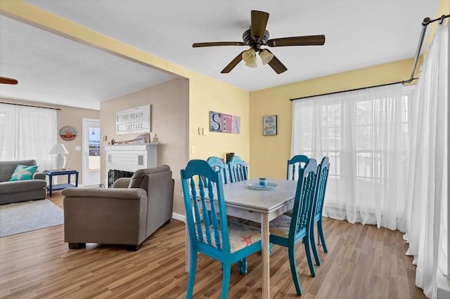 dining area with ceiling fan, a healthy amount of sunlight, a fireplace, and light hardwood / wood-style flooring