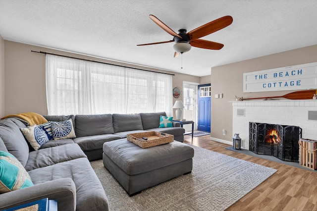 living room with a textured ceiling, a brick fireplace, wood-type flooring, and ceiling fan