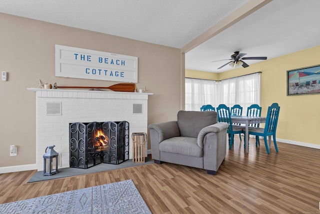 living room with ceiling fan, hardwood / wood-style floors, and a brick fireplace