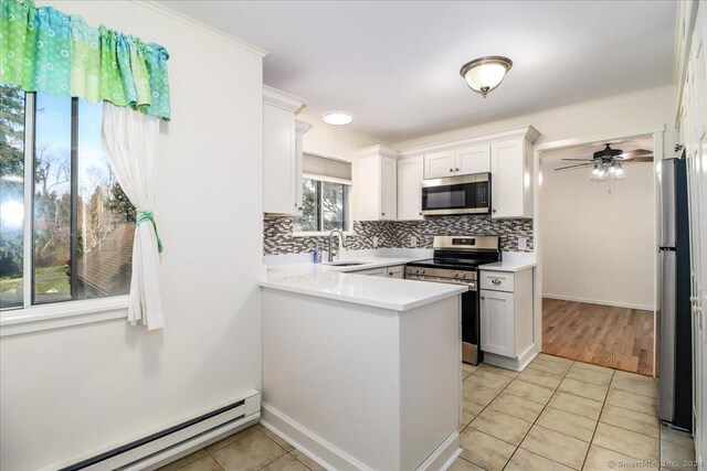 kitchen with white cabinetry, light tile patterned floors, baseboard heating, appliances with stainless steel finishes, and kitchen peninsula