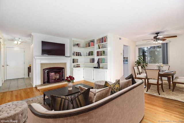 living room with crown molding, ceiling fan, light hardwood / wood-style floors, and a tile fireplace