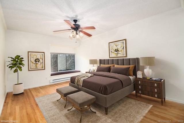 bedroom featuring a baseboard heating unit, light hardwood / wood-style flooring, a textured ceiling, and ceiling fan