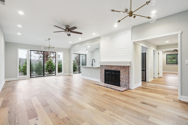 unfurnished living room with ceiling fan with notable chandelier, light hardwood / wood-style floors, and a fireplace