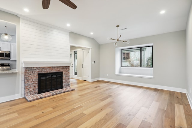 unfurnished living room featuring ceiling fan with notable chandelier, light hardwood / wood-style floors, a fireplace, and vaulted ceiling