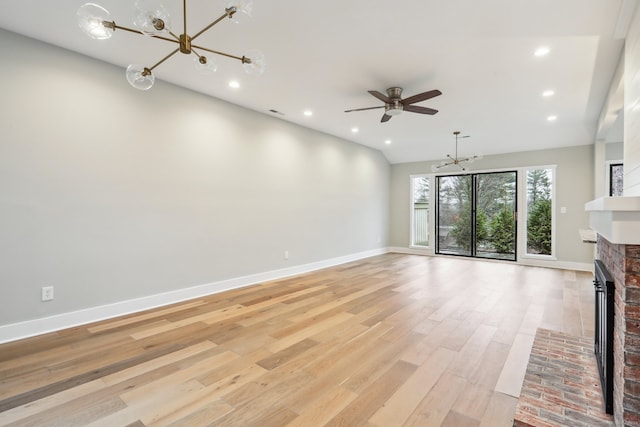 unfurnished living room with vaulted ceiling, a fireplace, ceiling fan with notable chandelier, and light wood-type flooring