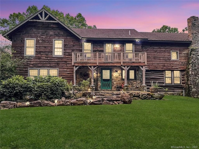 back house at dusk featuring a balcony and a yard