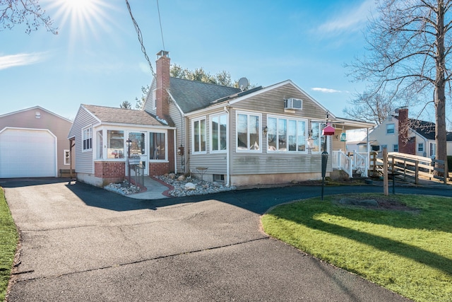 view of front of property featuring a sunroom, an outbuilding, a front lawn, and a garage