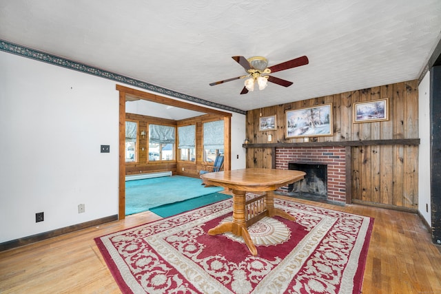 dining area with wood walls, hardwood / wood-style flooring, ceiling fan, a fireplace, and a baseboard radiator