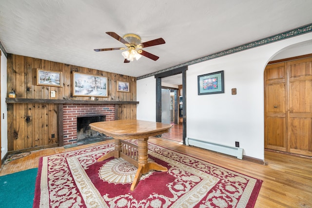 dining area featuring light wood-type flooring, a baseboard radiator, a brick fireplace, and ceiling fan