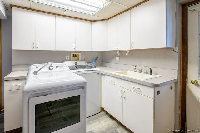 clothes washing area with cabinets, light wood-type flooring, washing machine and dryer, and sink