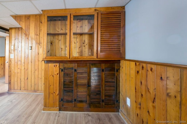 bar with wooden walls, a drop ceiling, and light hardwood / wood-style flooring