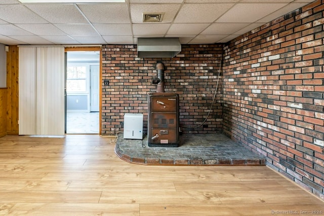 unfurnished living room with a paneled ceiling, brick wall, and light wood-type flooring