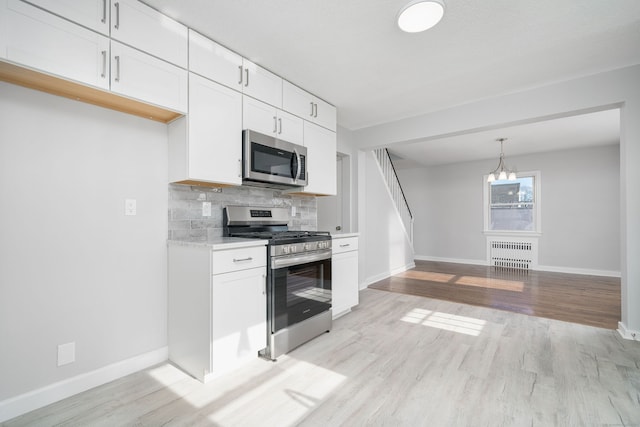 kitchen featuring radiator, white cabinetry, decorative light fixtures, appliances with stainless steel finishes, and light wood-type flooring