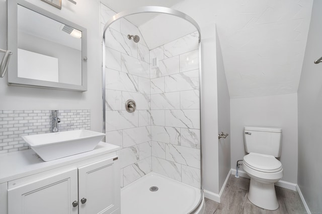 bathroom featuring vanity, hardwood / wood-style flooring, decorative backsplash, toilet, and tiled shower