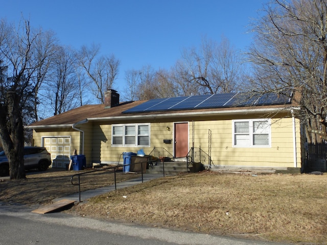 ranch-style home featuring a chimney, an attached garage, fence, and roof mounted solar panels