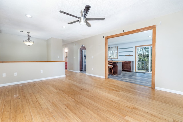 unfurnished living room featuring ceiling fan, a textured ceiling, and light hardwood / wood-style flooring