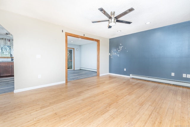 unfurnished room with ceiling fan, a baseboard radiator, and light wood-type flooring