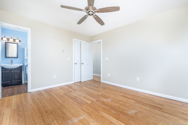 unfurnished bedroom featuring ensuite bath, ceiling fan, sink, hardwood / wood-style floors, and a textured ceiling