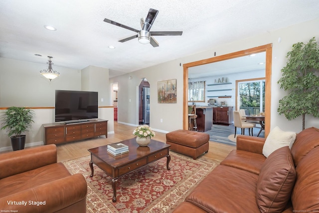 living room featuring ceiling fan, light hardwood / wood-style flooring, and a textured ceiling