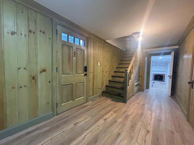 entrance foyer featuring a fireplace, wood walls, light wood-type flooring, and ornamental molding